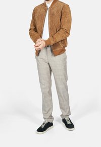 Bruine suède bomberjack met geribbelde kraag en cuffs, gecombineerd met lichtgrijze geruite broeken en zwarte sneakers met witte zolen.