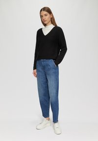 Zwarte V-halstrui, lichte geribde kraag, gecombineerd met lichtblauwe high-waisted denim broek. Witte platform sneakers. Eenvoudige achtergrond.