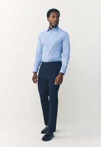 Camicia a righe azzurro chiaro con maniche lunghe, abbinata a pantaloni blu navy e scarpe di pelle nere, creando un outfit formale.
