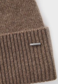Gorro de punto marrón con una textura acanalada, hecho de un material suave, con una etiqueta de logo en tono plateado cerca del dobladillo.