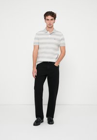 Camiseta polo a rayas en gris claro y blanco, con cuello y logo; combinada con pantalones negros de pierna recta y zapatos negros.