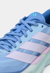 Baskets Adidas bleu clair avec des rayures lavande, des lacets assortis et une semelle vert menthe, montrant un gros plan de la partie supérieure et de la languette.