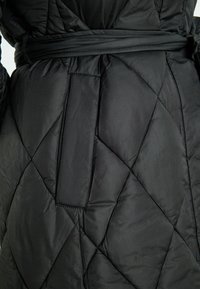 Gequilted zwarte jas met een gebogen taille, gemaakt van glanzende stof met een ruitvormig patroon en een gladde textuur.