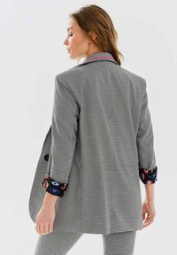 Čierno-biely kockovaný blejzer s voľným strihom, s farebnými vzorovanými akcentmi na manžetách a kontrastným detailom goliera.