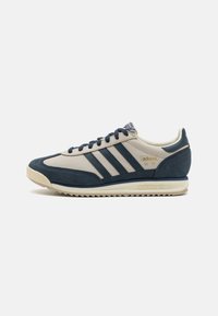 Marineblauwe suède en beige leren sneaker met drie strepen, ronde neus, gestructureerd oppervlak en een neutrale rubberen zool. Minimalistische branding op de tong.