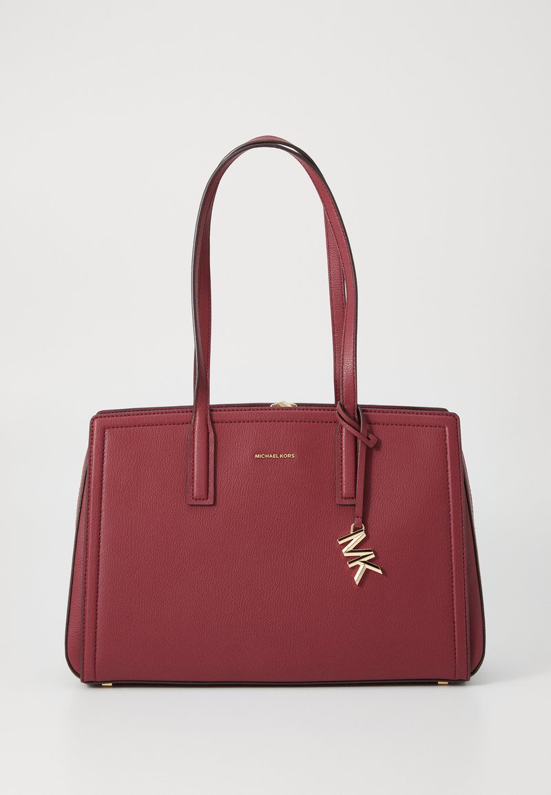 Sarkanu ādas somu ar strukturētu dizainu, dubultajām rokturiem un zeltainiem aksesuāriem. Iespējas ietver zelta logotipu un piekariņu ar iniciāļiem "MK".