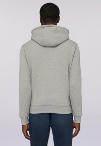 Grå hoodie med dragsko i huvan, ribbade muddar och resår i midjan. Mjuk textur med en avslappnad passform, bärs med mörka jeans.