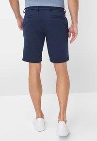Pantaloni corti blu navy realizzati in tessuto testurizzato, con due tasche posteriori e orlo dritto, abbinati a scarpe bianche slip-on.