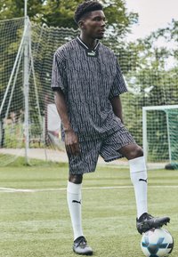 Svart och vit mönstrad sporttröja och shorts, med svart krage, tillsammans med vita strumpor och svarta fotbollsskor, på en gräsplan.