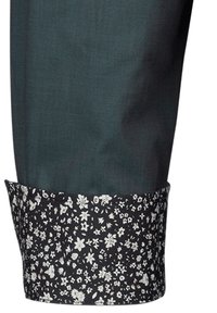 Pantalone di tessuto verde con un orlo floreale a contrasto in nero, caratterizzato da un motivo floreale bianco, texture morbida e design strutturato.