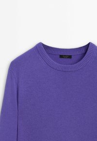 Pull en maille violet à col rond côtelé et manches longues, mettant l'accent sur le haut du torse sur un fond neutre.