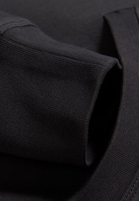 Tela de algodón negra que muestra una textura acanalada y un borde de puño plegado. Las costuras son visibles a lo largo de los bordes, destacando el diseño de la prenda.