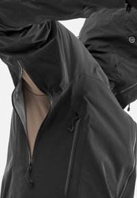 Veste légère noire avec une fermeture éclair à l'avant, poche angulaire et texture lisse avec un design ajusté. L'intérieur est beige.