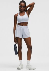 Top corto atlético de color azul claro con cremallera frontal, pantalones cortos ligeros a juego, zapatillas blancas y una botella de agua azul marino etiquetada "lululemon."