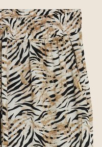 Shorts en imprimé animalier dans des teintes beige, noir et blanc. Tissu léger avec une taille élastique et un accent en métal doré.