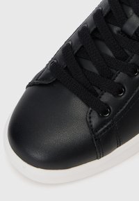 Black leather sneaker with flat black laces, rounded toe, and white rubber sole. Smooth texture with minimal stitching detail.