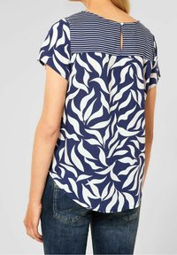 Kortärmad skjorta med marinblå bakgrund, vitt bladmönster och randig axel. Har en knappstängning i ryggen och en svängd nederkant.