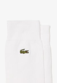Weiße Baumwollsocken mit geribbelter Textur. Verfügt über ein kleines grünes Krokodil-Logo an der Seite. Doppelte Bündchenkonstruktion für zusätzlichen Komfort.