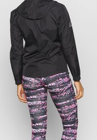 Svart, lätt jacka med huva, kombinerad med figurnära leggings med ett svart och rosa abstrakt mönster. Texturerade material syns.