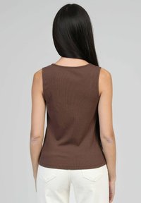 Débardeur marron sans manches en tissu côtelé, avec un col rond. Porté avec un pantalon clair, mettant en valeur une silhouette ajustée.