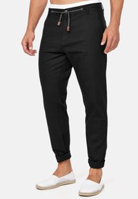 Pantalon en mélange de coton noir à coupe effilée, avec un cordon tressé à la taille et des revers roulés, associé à des chaussures blanches à enfiler.
