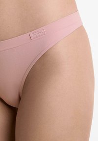 Roze stringondergoed met een gladde textuur, gemaakt van elastische stof. Kenmerkt zich door een dunne tailleband en een zichtbaar logo-label.