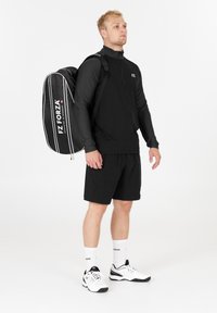 Musta pitkähihaisten puuvillapaitojen neljänneksen vetoketjulla, yhteensopivat shortsit ja valkoiset urheilukengät. Mustassa reppu on valkoisia raitoja ja logo. Minimalistinen muotoilu.