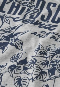 Tela gris con una apariencia texturizada, que presenta un diseño floral en azul marino de hojas y texto estilizado en una fuente de contraste.