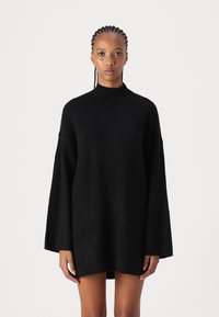 Black oversized sweater dress with a high neckline and wide sleeves, featuring a textured knit fabric and a loose fit.