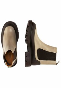 Stivaletti beige in pelle con suola in gomma marrone scuro, pannelli laterali elastici e linguetta di aiuto. Presentano dettagli testurizzati sulla suola.