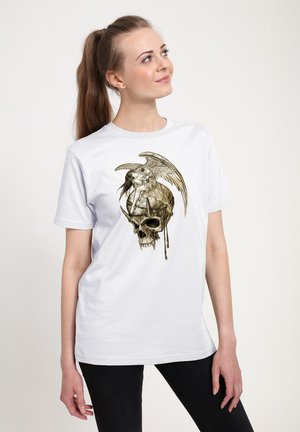 Ung kvinde iført en hvid t-shirt med detaljeret tryk af en bevinget kvindelig figur, der sidder på en hjelm med horn.