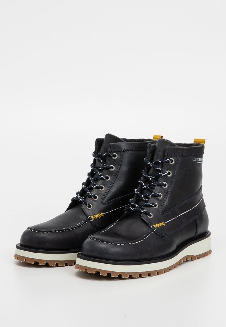 Bottes en cuir noir avec un col rembourré, des coutures blanches et des lacets bleus. Elles possèdent une semelle robuste avec des accents marron et un onglet de talon jaune.