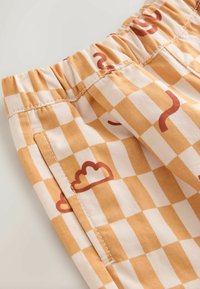 Kostkované látkové šortky v oranžové a krémové barvě. Mají elastický pas a hravé vzory oblaků a křivek. Měkká bavlněná textura.