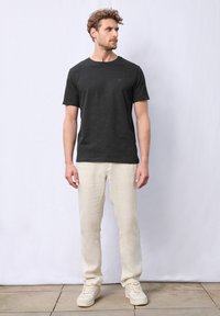 Svart kortärmad t-shirt, rak passform, bärs med ljus beige linnebyxor och vita sneakers. Lätt textur, minimalistisk design, inga mönster.