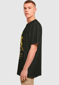 Sort bomulds t-shirt med et grafisk design i gul og grøn med tekst, en løs pasform, korte ærmer og rund halsudskæring.
