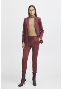 Bourgogne blazer med två fickor över en tan turtleneck, matchat med joggerbyxor och bruna högklackade stövlar. Slät tygtextur.