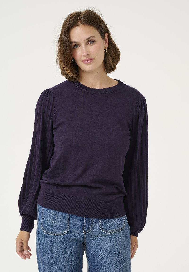 Lila Pullover mit langen, plissierten Ärmeln und einem Rundhalsausschnitt, kombiniert mit blauen Jeans. Weiche Textur, tailliert.
