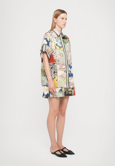 Multi-patterned short-sleeve shirt with floral and geometric designs in vibrant colors, paired with a matching patterned skirt and black flats.