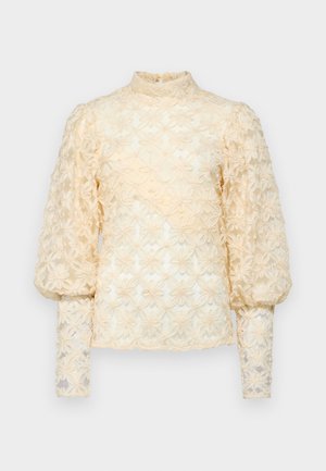 Blouse en lin brodé de fleurs de couleur beige clair. Caractérisée par des manches longues bouffantes et un col haut à volants. Motifs floraux délicats et texturés sur l'ensemble.