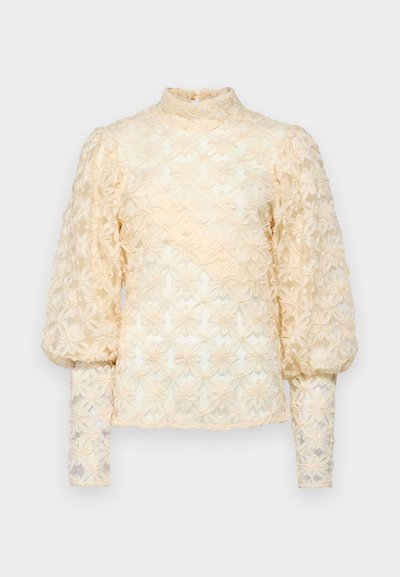 Blomsterbrodert bluse i lys beige. Har lange, puffete ermer og en rynket høy hals. Delikate, teksturerte blomsterdesign over hele.