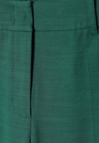 Groene stof met een gladde textuur, met een vlakke voorkant, subtiele verticale lijnen en een tailleband met stikseldetails.