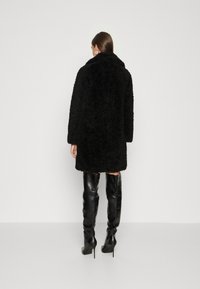 Cappotto in pelliccia sintetica nera con vestibilità comoda, maniche lunghe e ampio colletto, abbinato a stivali in pelle nera alti fino alla coscia.
