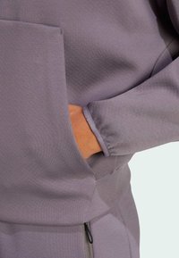 Felpa viola con cappuccio, dotata di tasca frontale, tessuto testurizzato, maniche a soffietto e dettagli con coulisse in vita. Design morbido e casual.