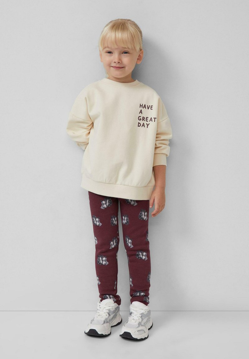 Kremowy sweatshirt z napisem "MIŁEGO DNIA", w połączeniu z burgundowymi legginsami z wzorem wilka, uzupełniony białymi sneakersami.