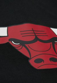 Tissu noir avec un logo de taureau rouge. Le design comprend des accents blancs et des contours noirs, mettant en valeur une texture graphique lisse.