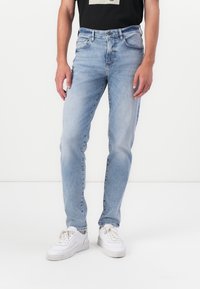 Pantalones vaqueros de mezclilla azul claro con corte slim, diseño de cinco bolsillos y un acabado ligeramente descolorido, combinados con zapatillas blancas.