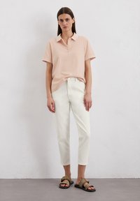 Lichtroze poloshirt met korte mouwen, witte cropped broek en bruine sandalen met een zwarte zool. Eenvoudig ontwerp, gladde textuur.
