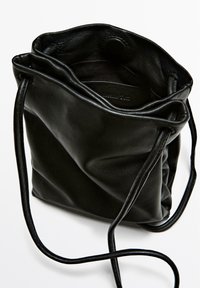 Sort læder rygsæk med blød tekstur, slank skulderrem og en indvendig design ved åbningen. Har en trykknaplukning.