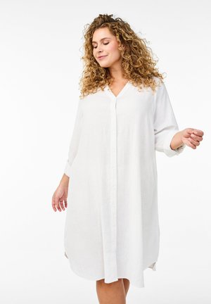 White linen shirt dress with a V-neck, button front, and long sleeves. Features side slits and a relaxed fit, gently flowing to mid-thigh.
