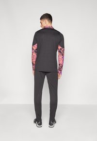 Long-sleeve black athletic top with colorful, abstract-patterned sleeves, paired with black pants and black athletic shoes.